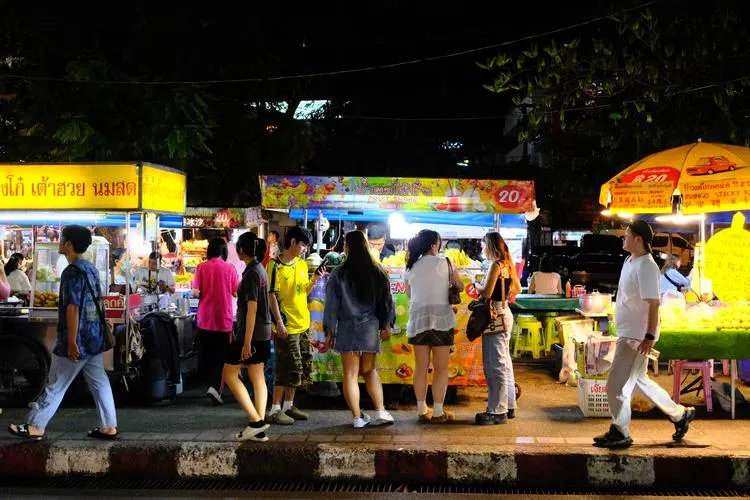 Crowds strolling through a busy night market lit by food stall signs