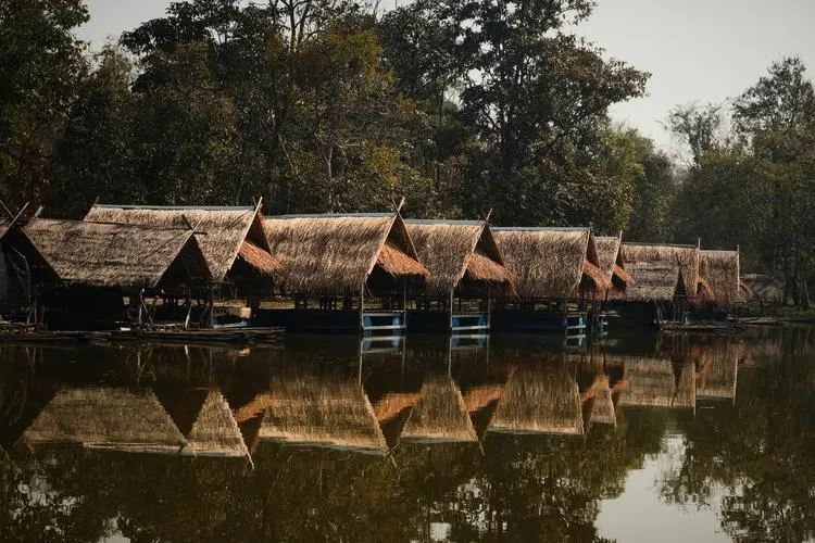 Bamboo huts with thatched roofs lined up along a calm lake